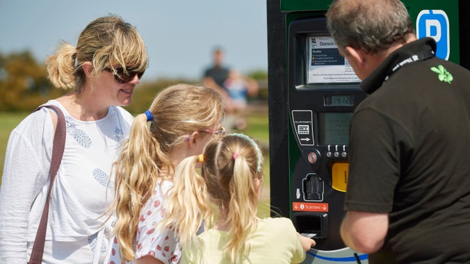 Volunteer helping visitors with the car park ticket machine at Dunwich Heath and Beach, Suffolk